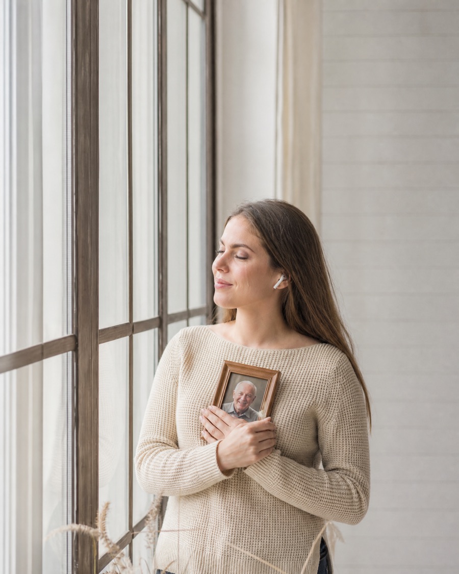A young woman with earbuds in, holding a photo of her grandfather while his song plays
